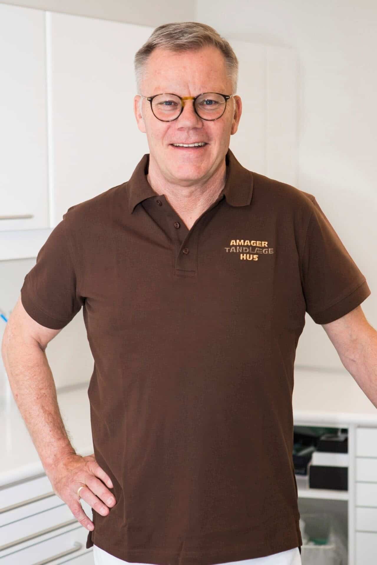 Smilende mandlig tandlæge i brun uniform fra Amager Tandlægehus.