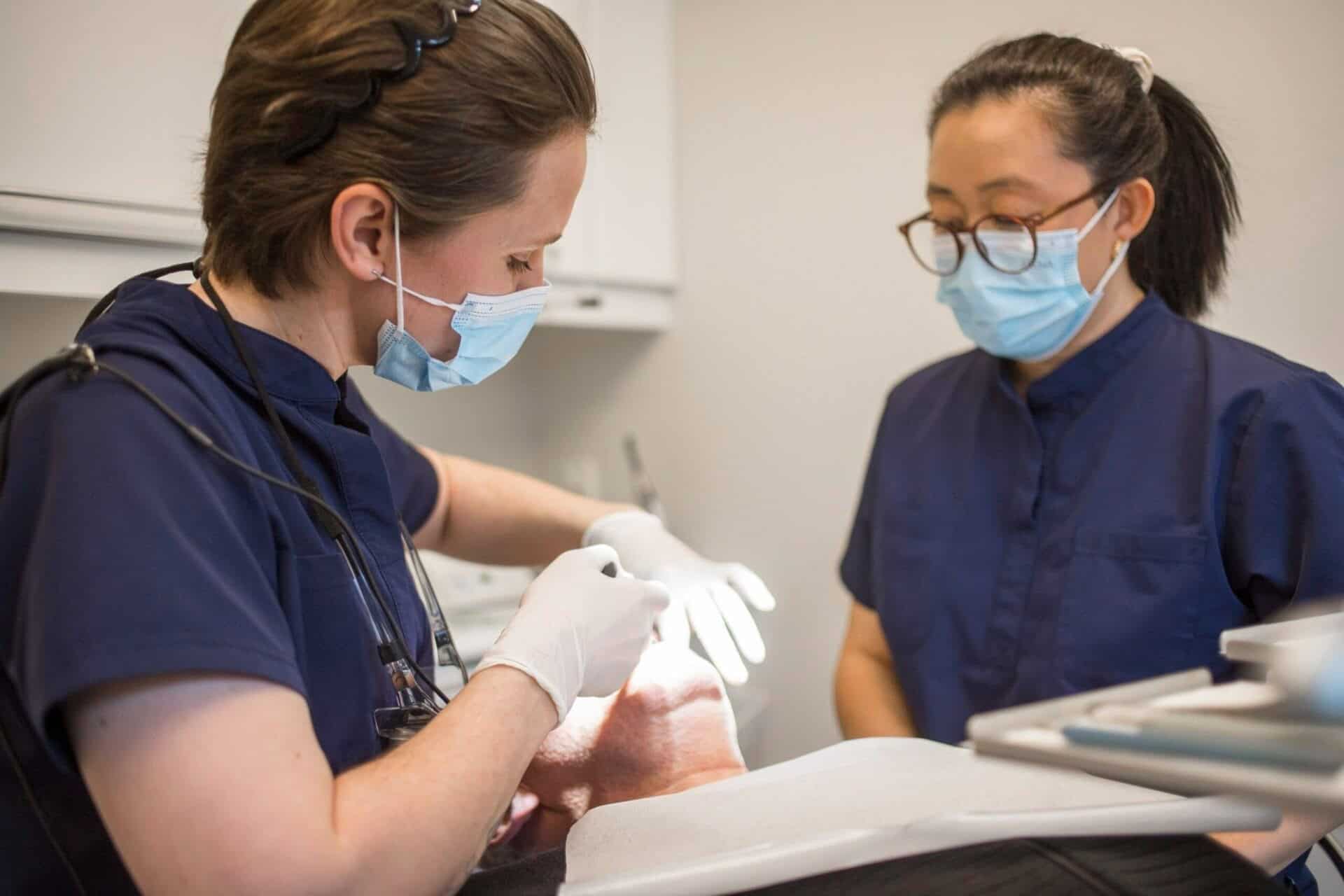 Kvindelig tandlæge og klinikassistent udfører tandbehandling på patient.